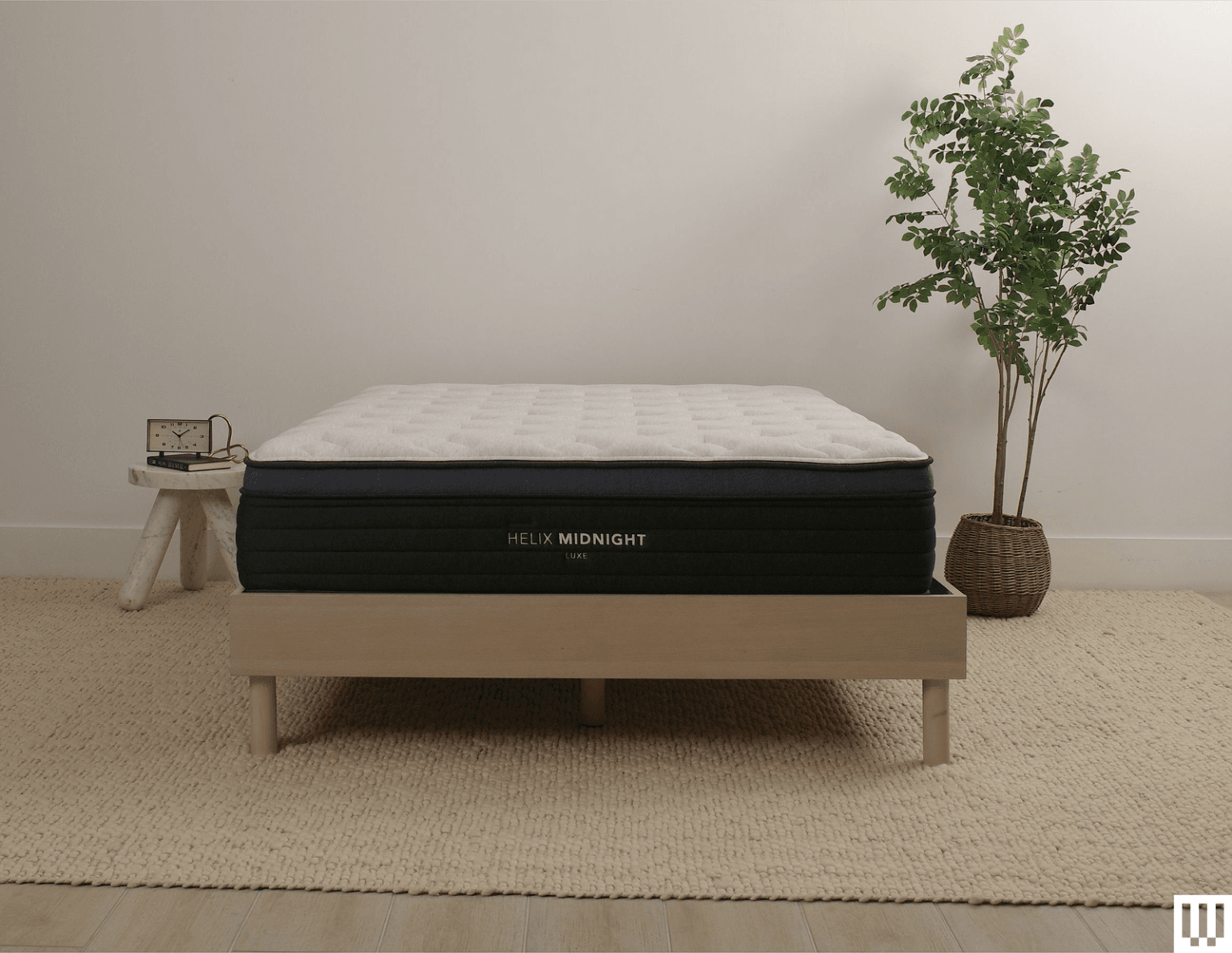 Helix Sleep Midnight Luxe a white mattress with blue trim on a minimalist wooden frame with a nightstand and potted...